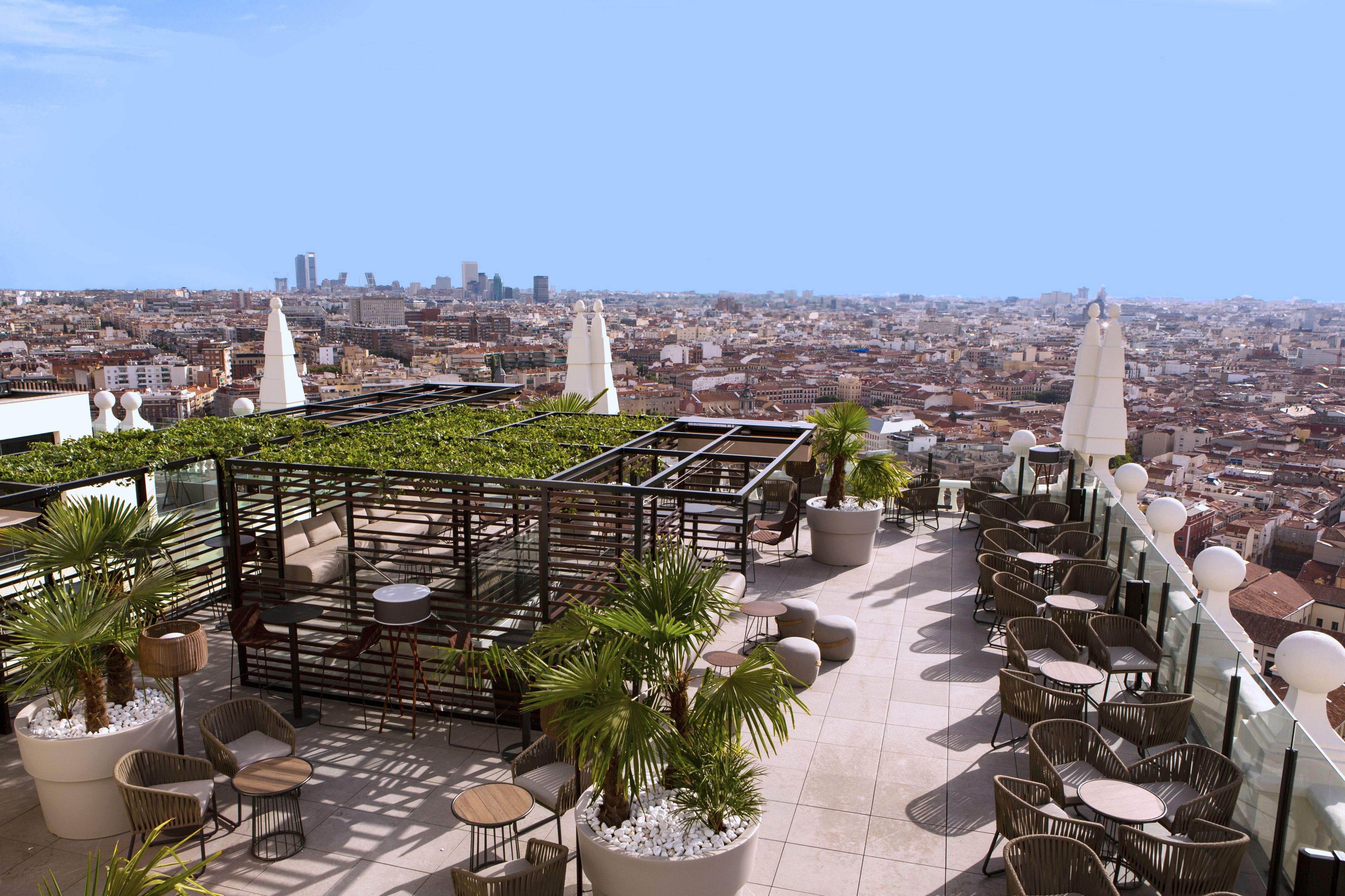 A rooftop terrace with outdoor seating, potted plants, and a city view.