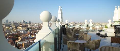 Terraza en la azotea con sillas y mesas de mimbre, con vistas panorámicas de la ciudad.