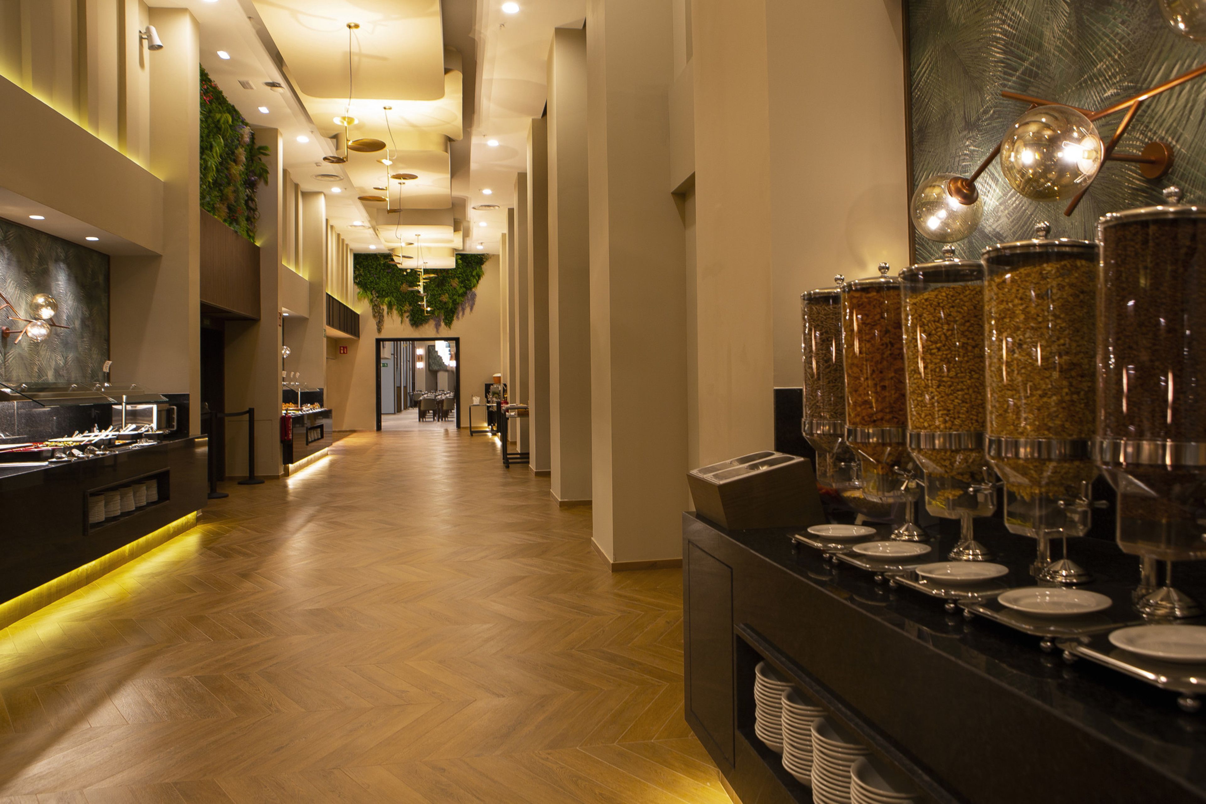Un couloir d’hôtel avec un espace buffet où l’on trouve des plats présentés dans des récipients en verre, ainsi qu’un long plancher en bois.