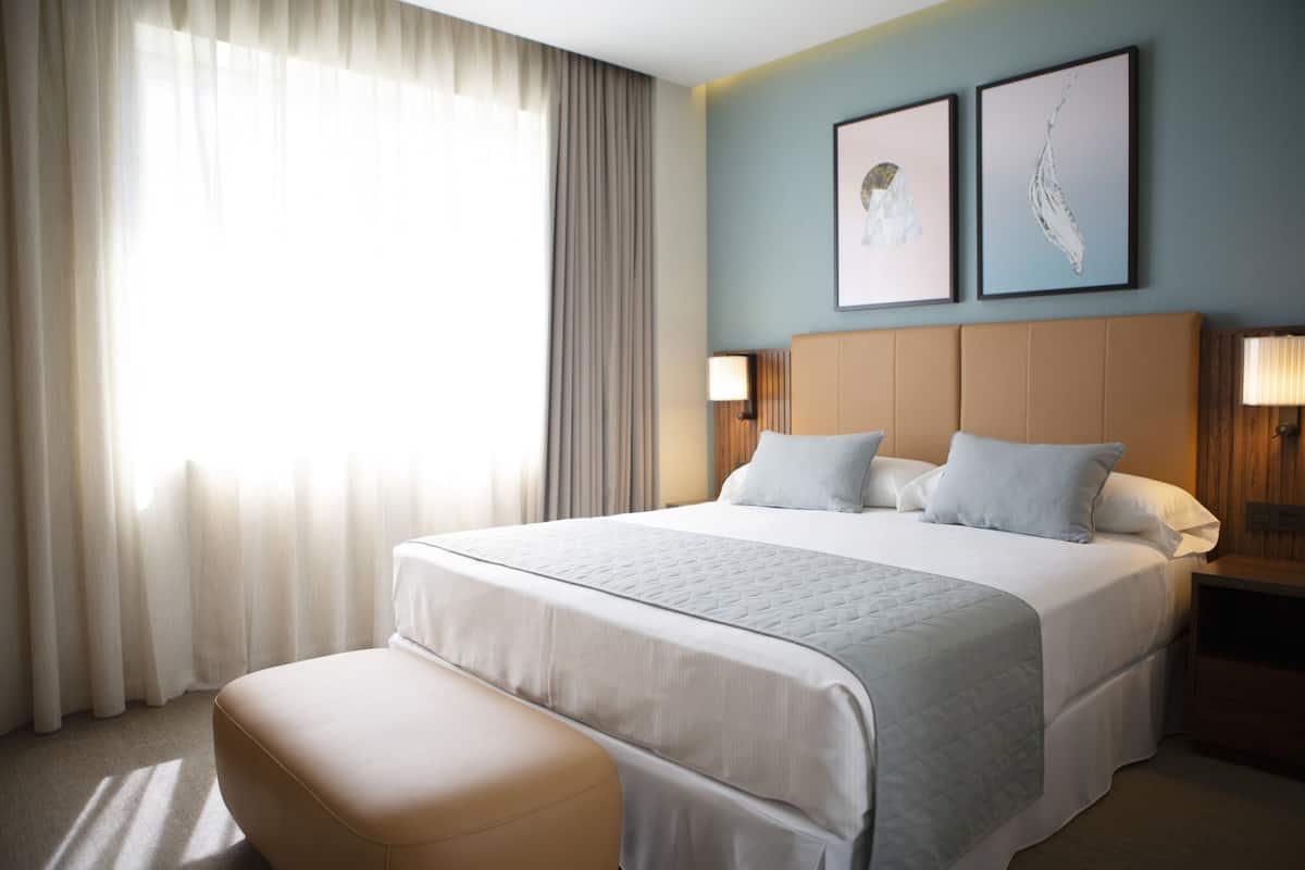 A hotel room with a large bed, a bench, two bedside tables, and a window with curtains.