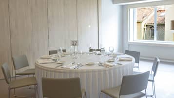 Un tavolo da pranzo rotondo con posti a sedere numerati, circondato da sedie, in una stanza con un'ampia finestra e vista su un edificio con tetto in tegole.