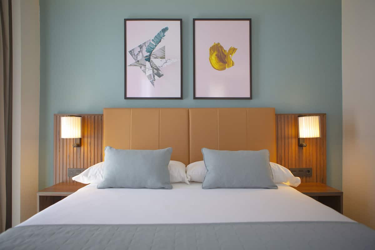 A hotel room with a large bed, two side tables, and two wall-mounted lamps.