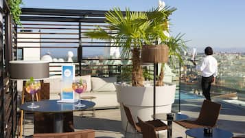 A rooftop terrace with outdoor seating, a large potted plant, and a city view.