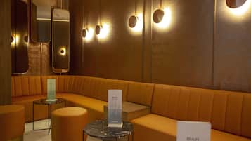 A modern bar area with a curved orange seating arrangement, a small round table, and a mirror with lights.