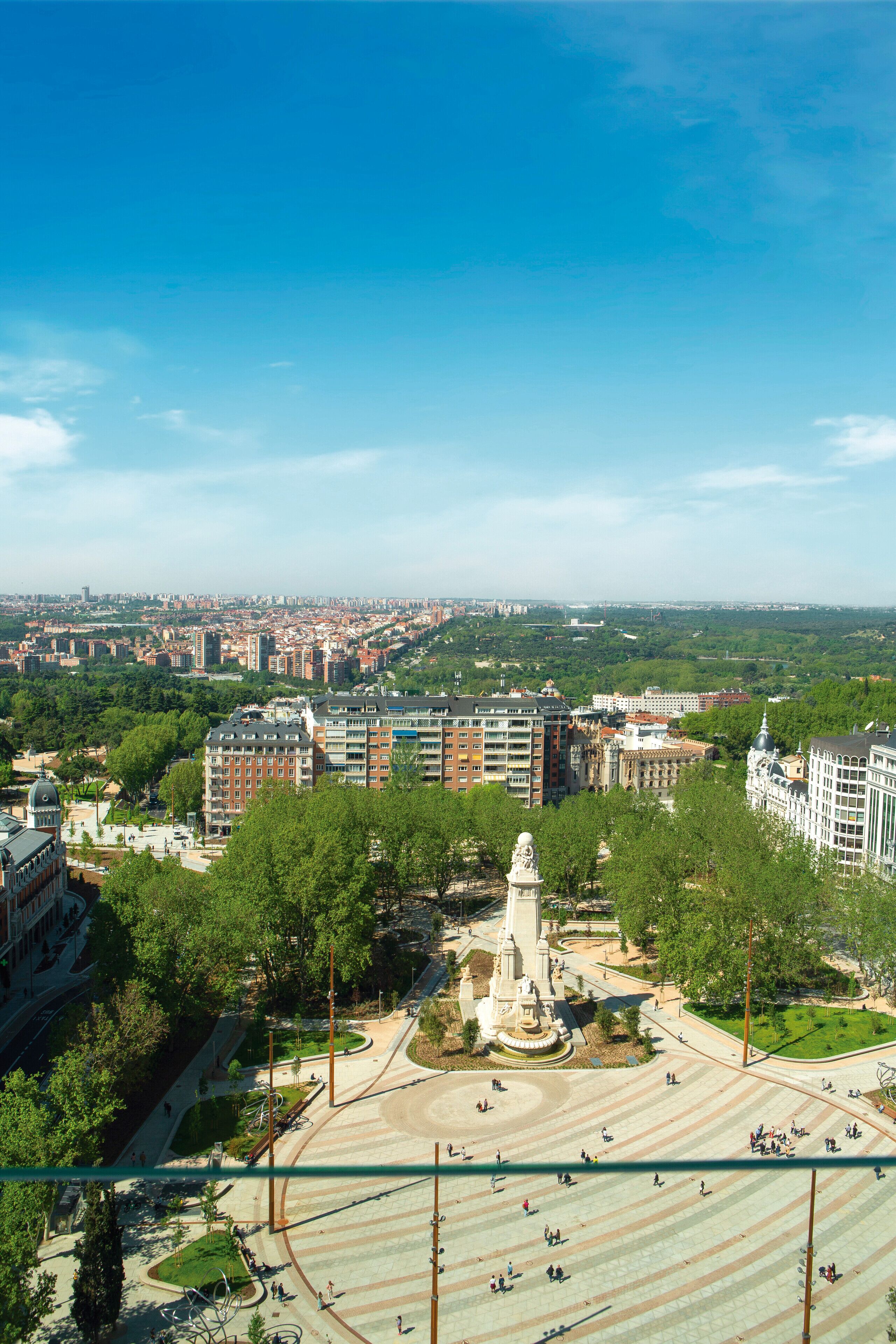 Uma praça com um monumento central, rodeada por edifícios e vegetação.