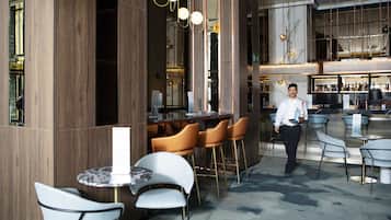 Zona de bar moderna con paredes de madera, mesas de mármol y sillas contemporáneas.