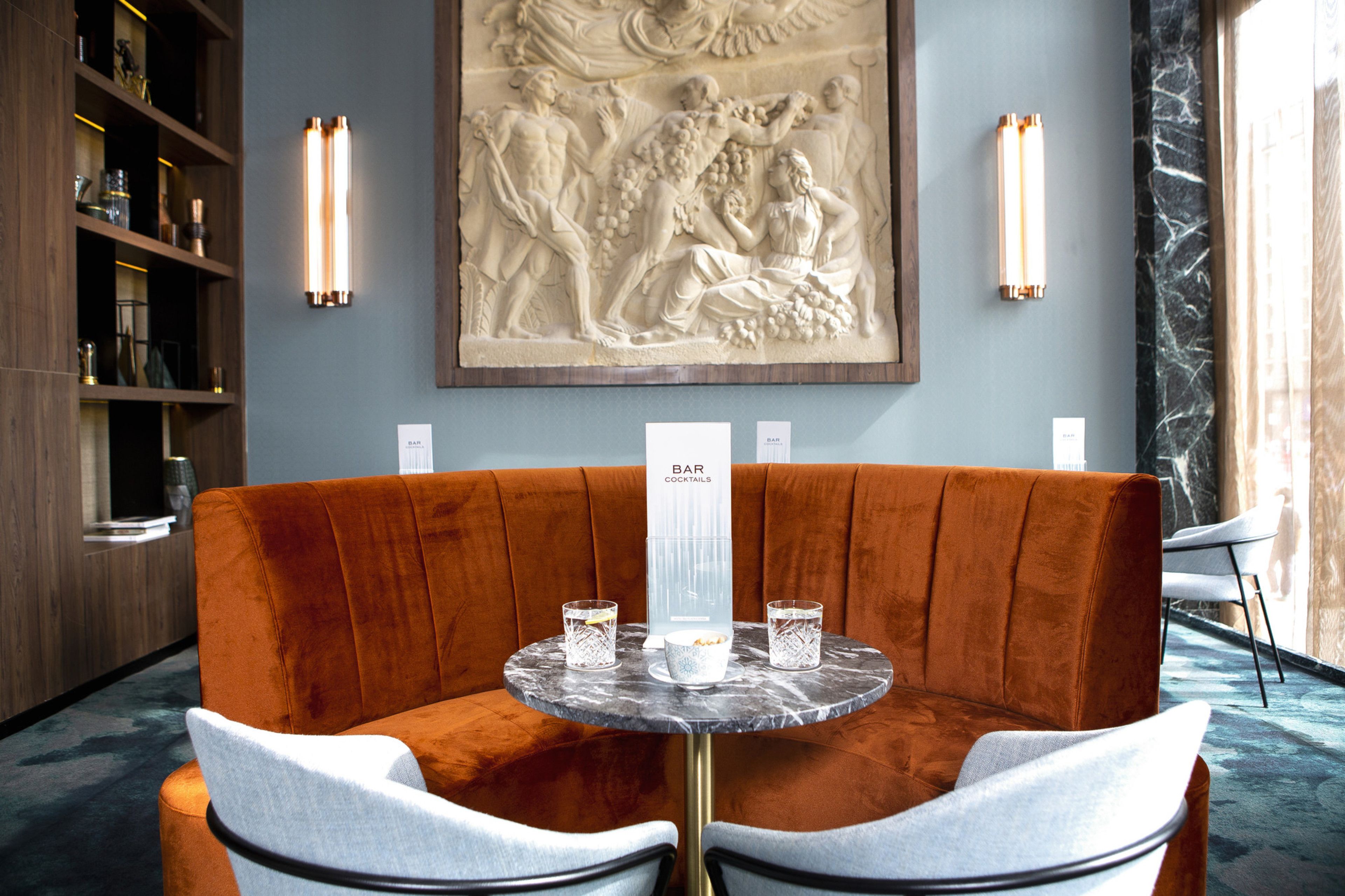 Un área de bar moderna con una mesa de mármol, dos sillas acolchadas y una gran escultura en relieve en la pared.