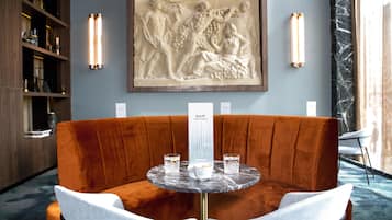 Un área de bar moderna con una mesa de mármol, dos sillas acolchadas y una gran escultura en relieve en la pared.