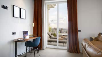Una habitación de hotel moderna con un escritorio, una silla azul, un sofá de cuero marrón y un balcón con vistas.