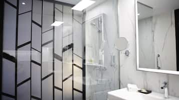 A modern bathroom with a glass-enclosed shower, a marble wall, a round mirror, and a white sink with a soap dish.
