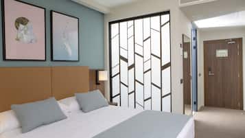 Une chambre d’hôtel avec un lit, deux oreillers, une tête de lit, une lampe fixée au mur et deux tableaux encadrés.