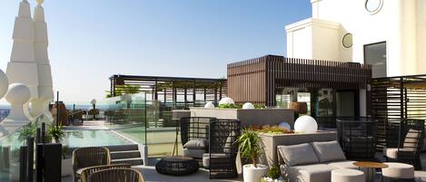 A rooftop terrace with outdoor seating, a pool, and a view of a tower.