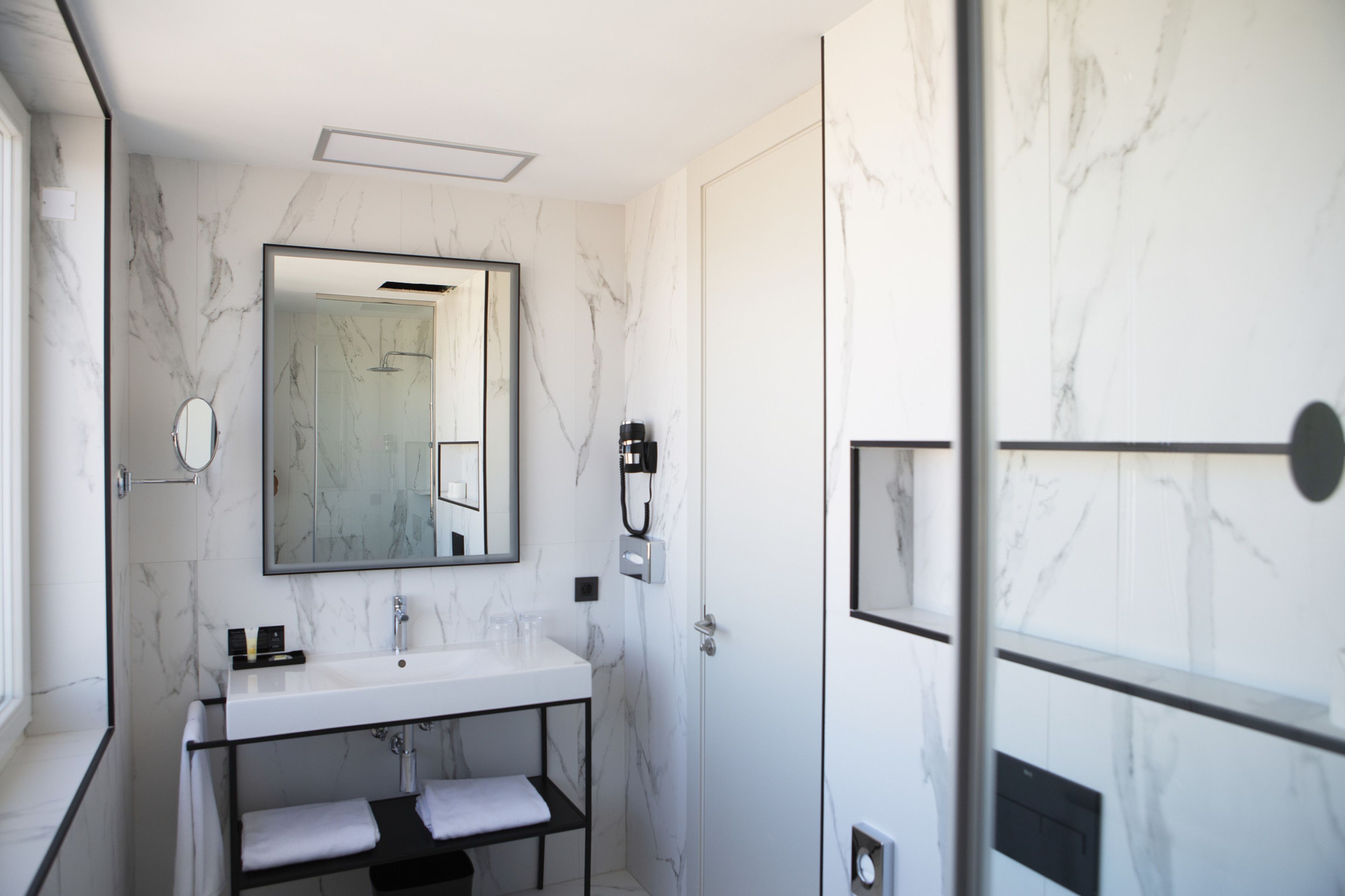 Un baño moderno con pared de mármol blanco, un espejo grande, un lavamanos y una ducha.