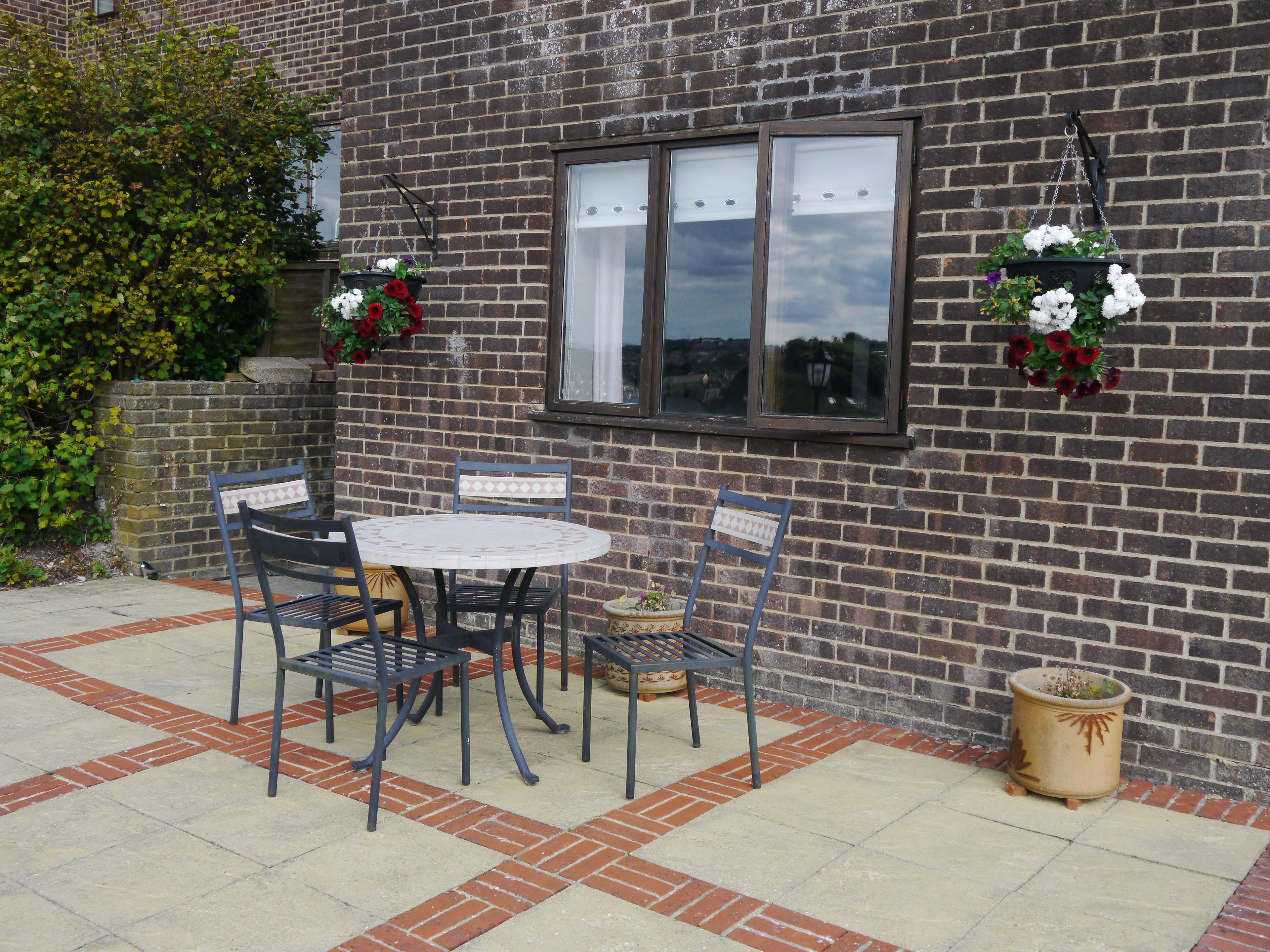 A patio with a round table and four chairs, a brick wall, and hanging flower baskets.