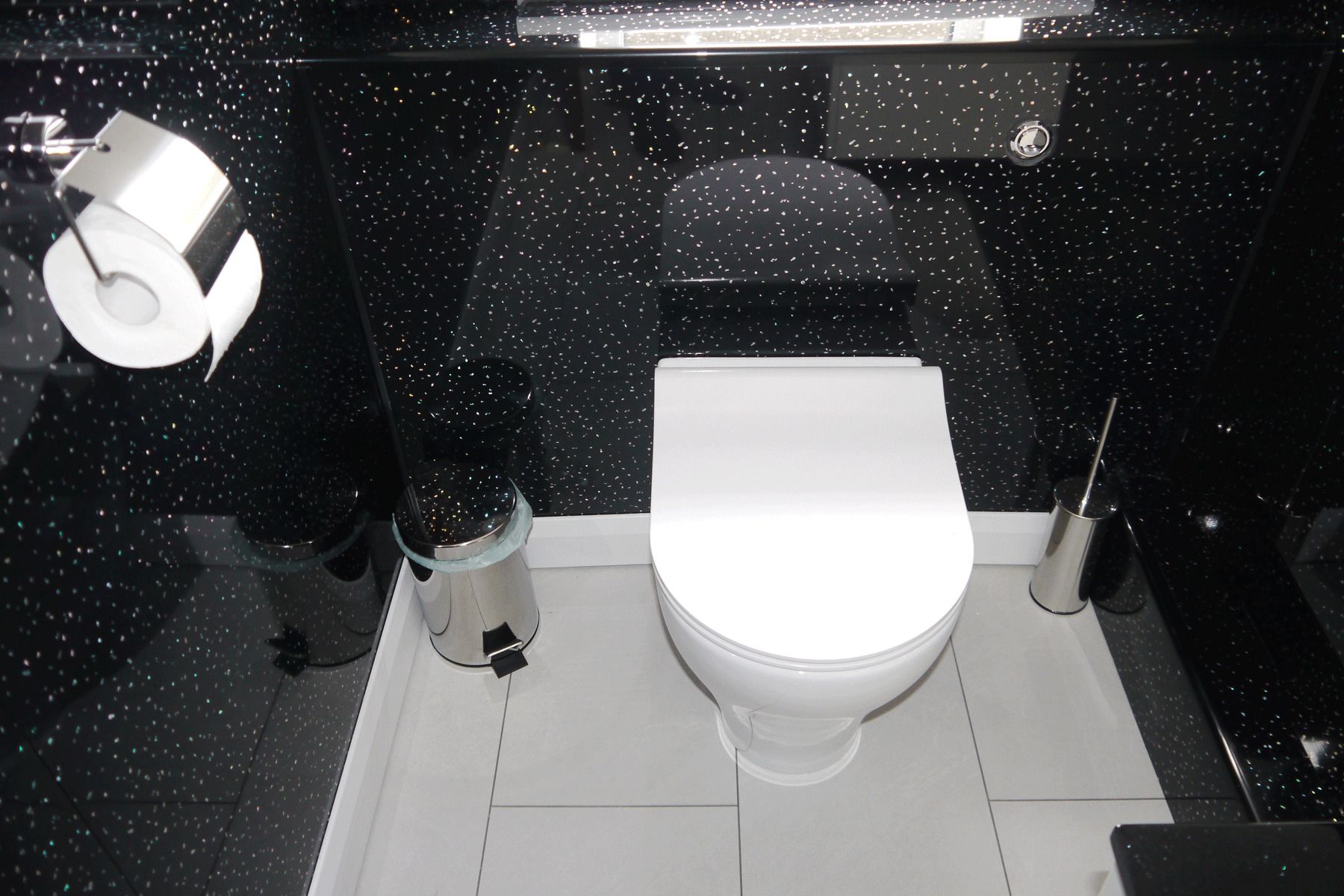 Un baño moderno con inodoro, un bote de basura y un dispensador de papel higiénico.