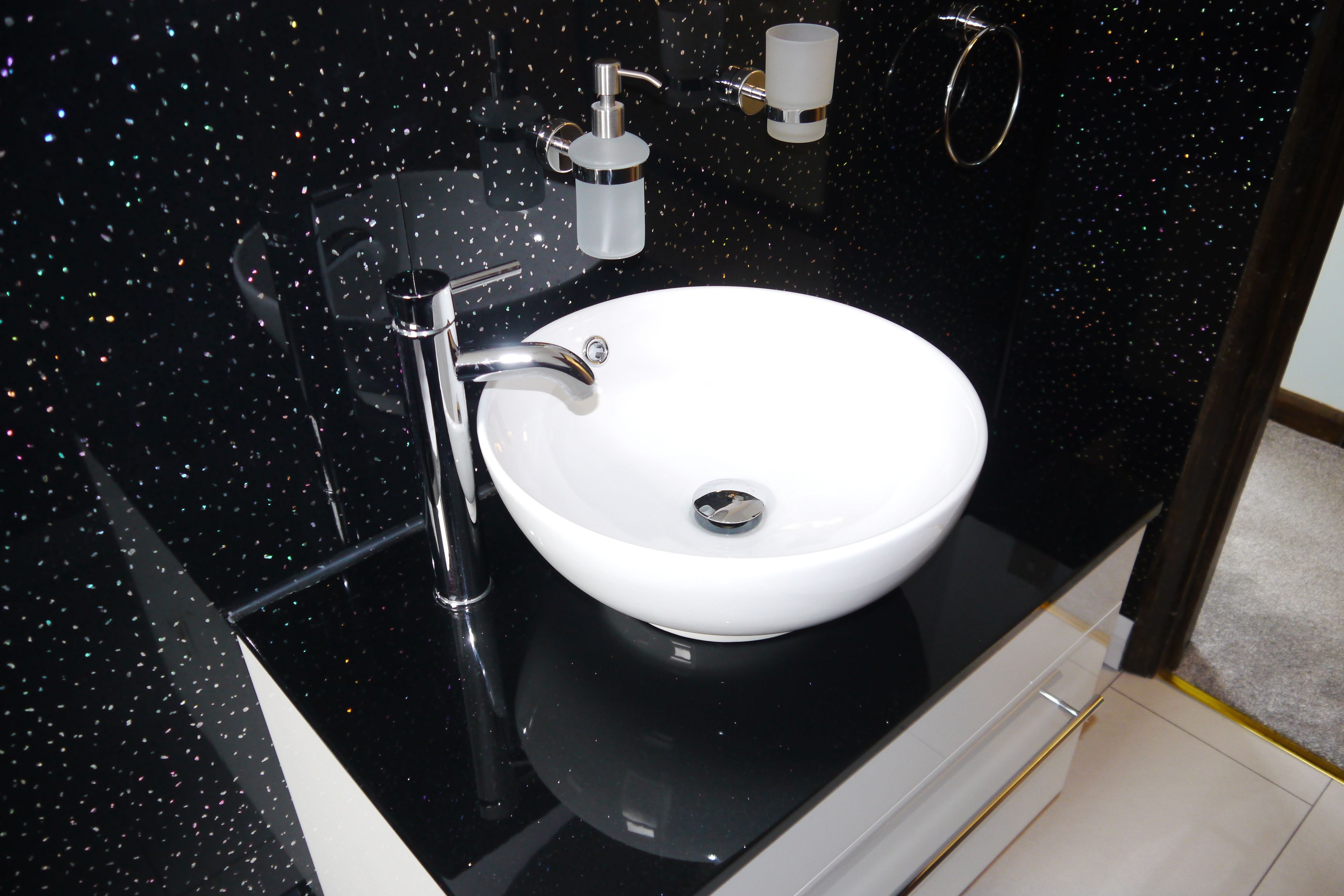 A modern bathroom with a white sink, chrome faucet, and a black speckled backsplash.