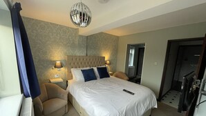 A hotel room with a large bed, two bedside lamps, a ceiling light, a radiator, and a door leading to another room. - Heathwood BnB (Dover)