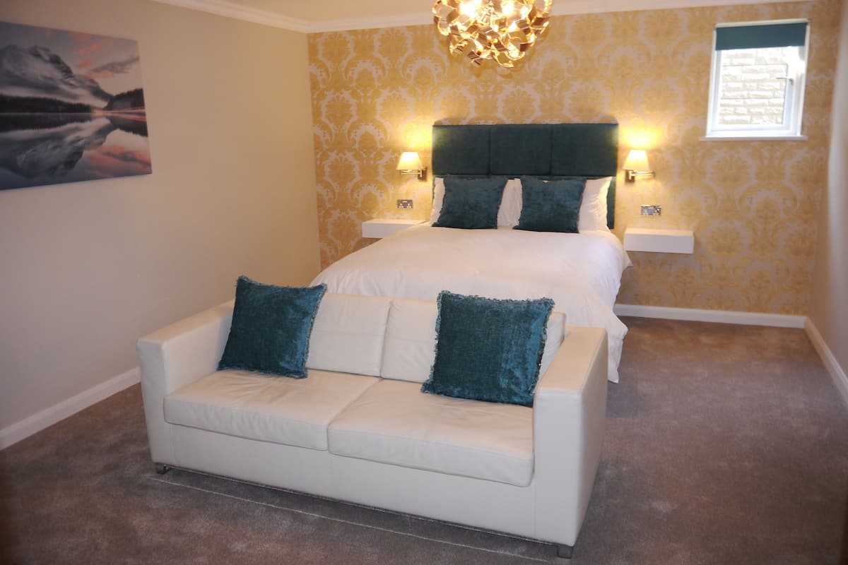 A bedroom with a bed, a white sofa, and a painting on the wall.