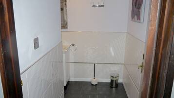 Ein Badezimmer mit weißen Fliesenwänden, dunklem Boden, Toilette, Mülleimer, Handtuchhalter und Spiegel.