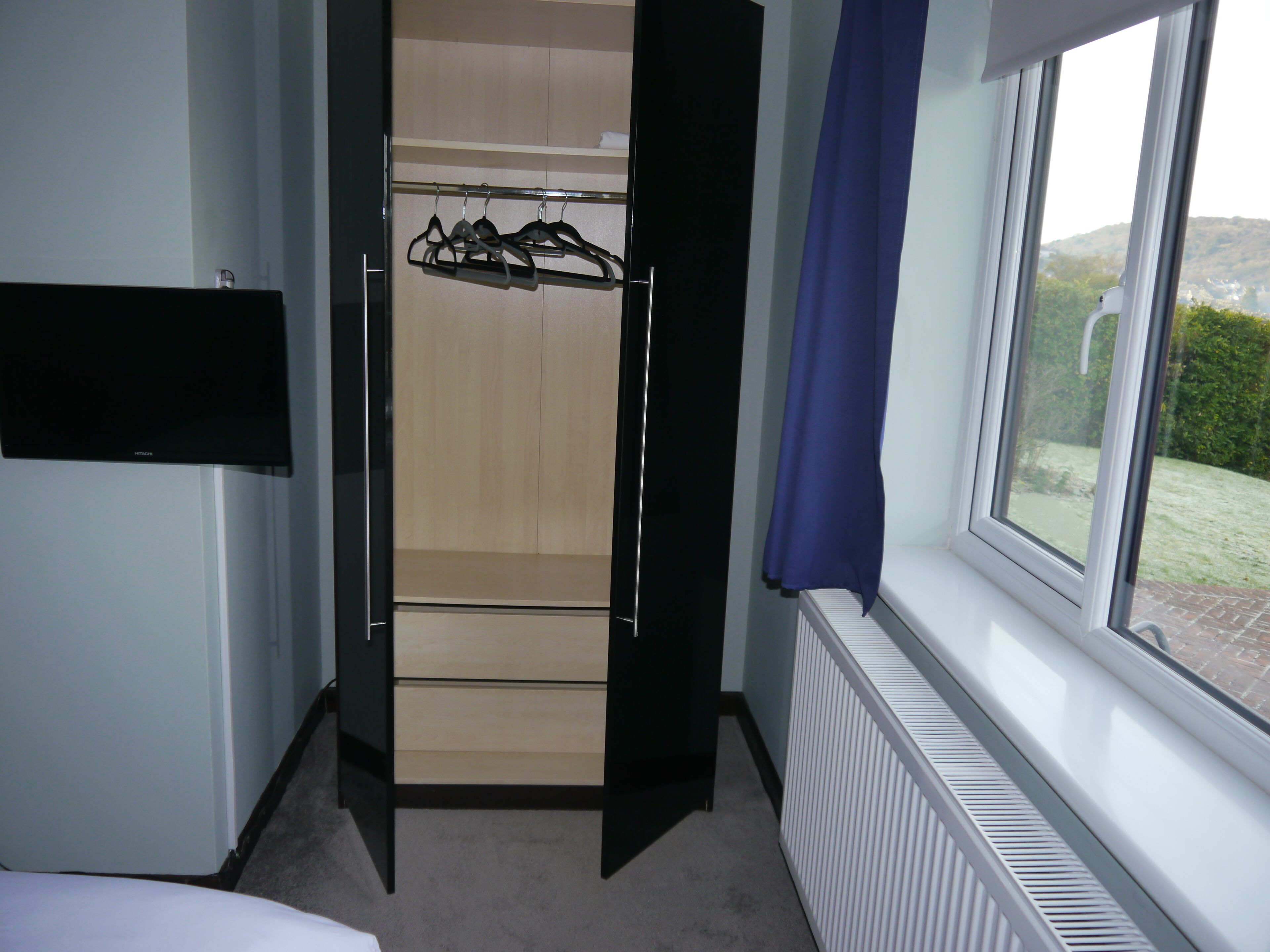 Een slaapkamer met een kledingkast, een radiator en een raam met uitzicht op groen.