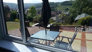 A patio with a table and chairs, a black umbrella, and a view of a residential area with houses and greenery. - Heathwood BnB (Dover)