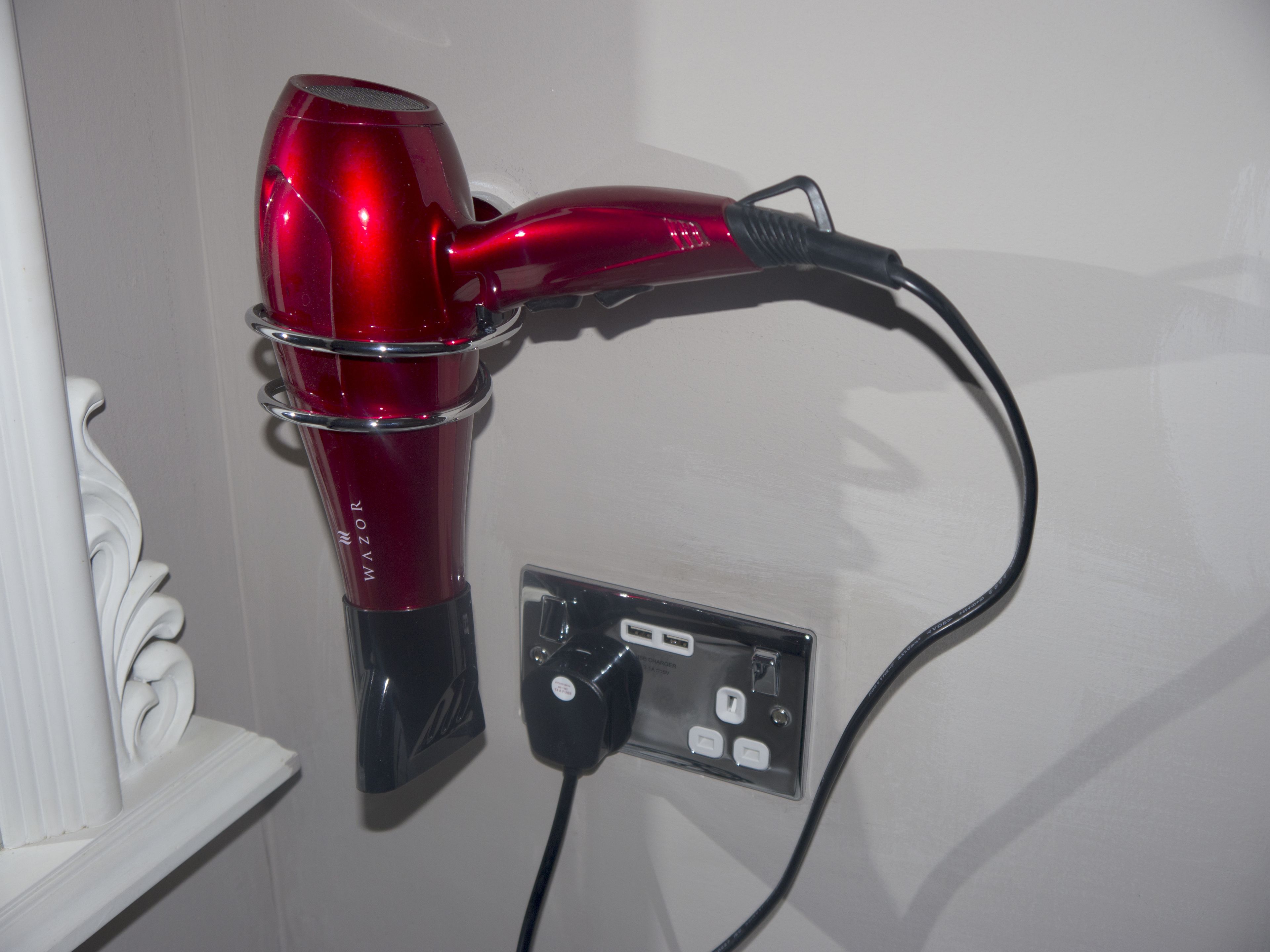 A red hair dryer mounted on a wall, connected to a power outlet.