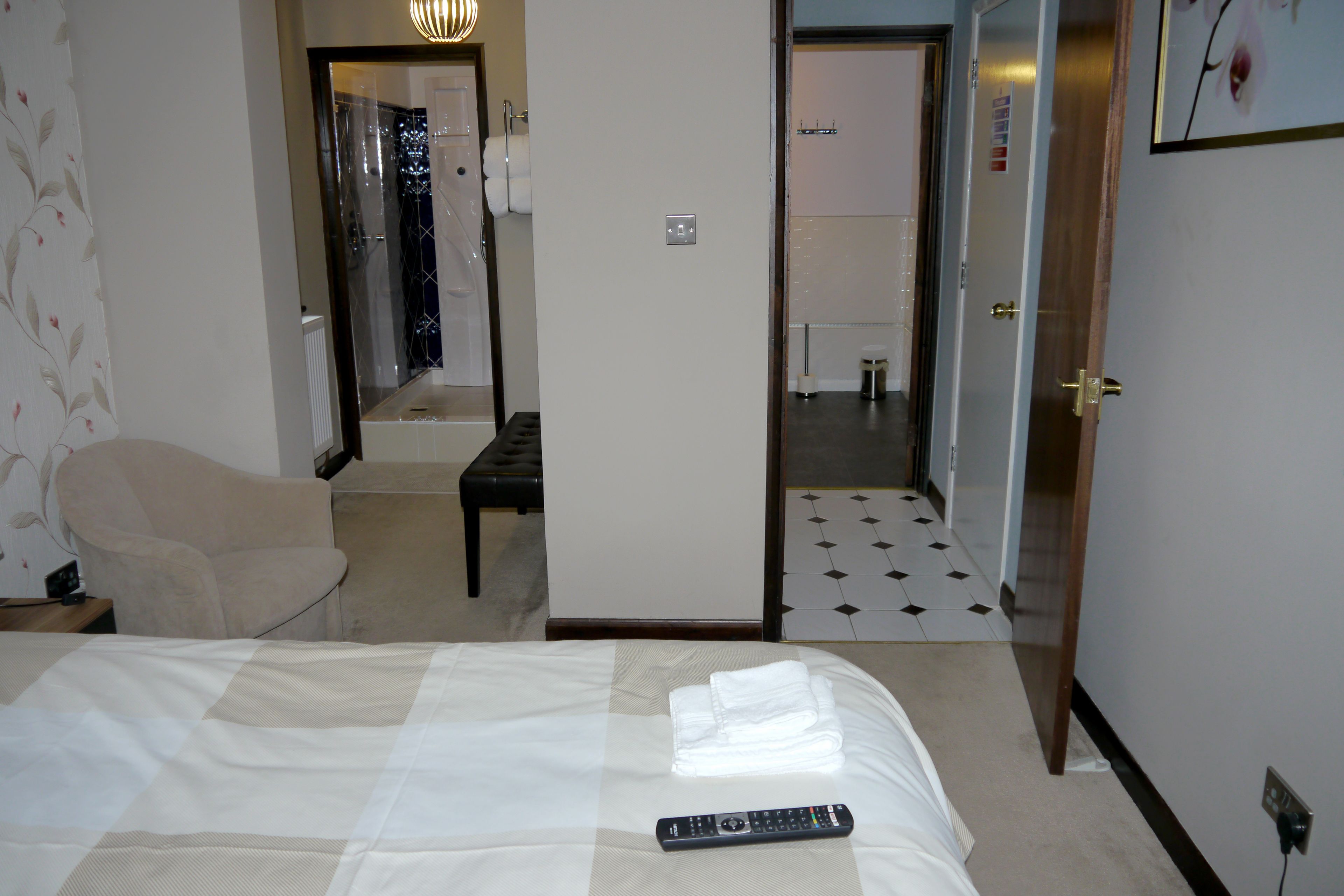 Une chambre d’hôtel avec un lit, une chaise, une télécommande et une salle de bain visible à travers une porte ouverte.