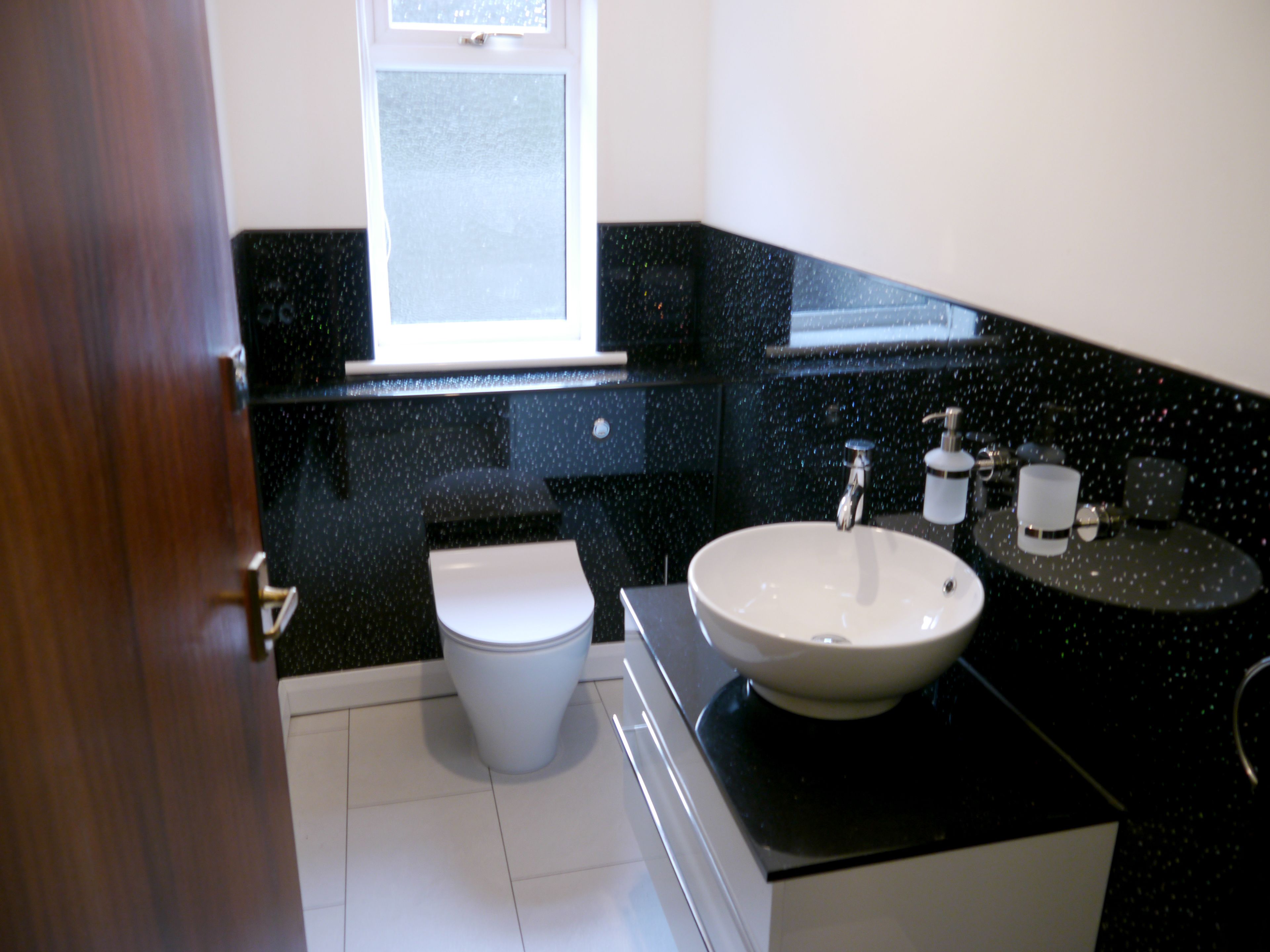 Baño con inodoro blanco, lavamanos y ventana sobre el espejo.