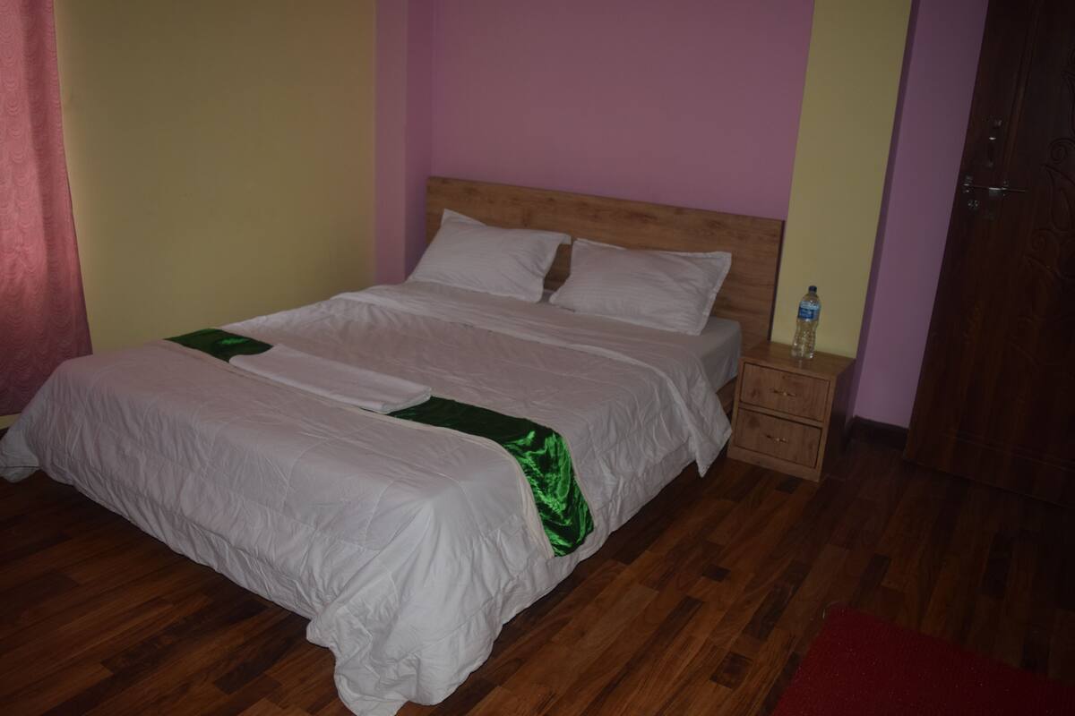 A bed with white bedding and a green accent, a wooden nightstand with a bottle, and a wooden floor.