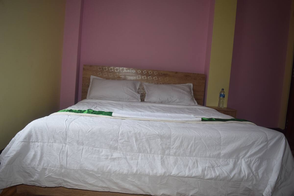 A bed with white bedding and a wooden headboard, a bedside table with a bottle, and a wall with a vertical stripe pattern.