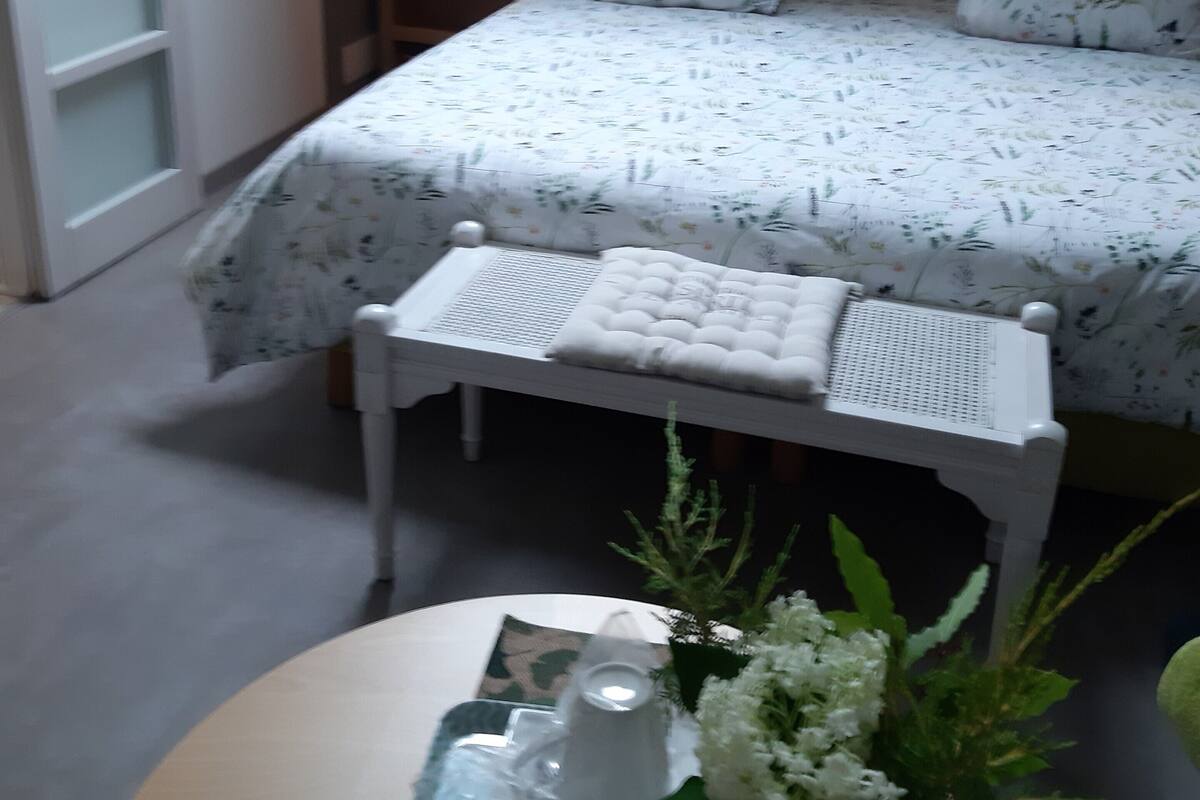 A bedroom with a bed, bedside tables, a bench, and a small table with a vase of flowers.