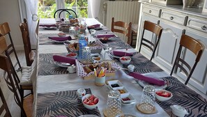 Une table à manger dressée avec différents plats, des verres et des couverts, entourée de chaises en bois.