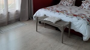 Une chambre à coucher avec un lit, une banquette, une table de chevet et une fenêtre avec des rideaux.