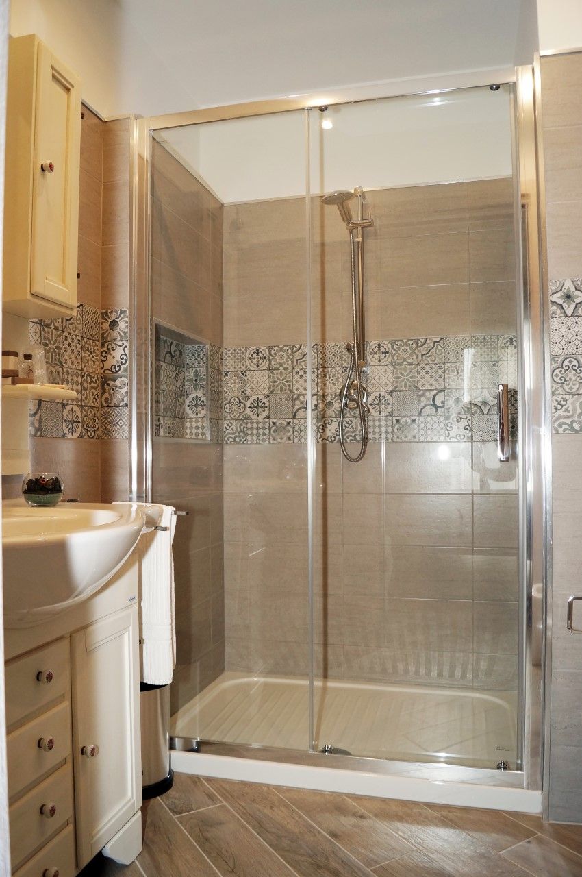 A modern bathroom with a glass-enclosed shower, a vanity with a sink, and patterned tiles on the walls.