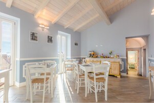 Comedor con mobiliario blanco y una cocina al fondo.