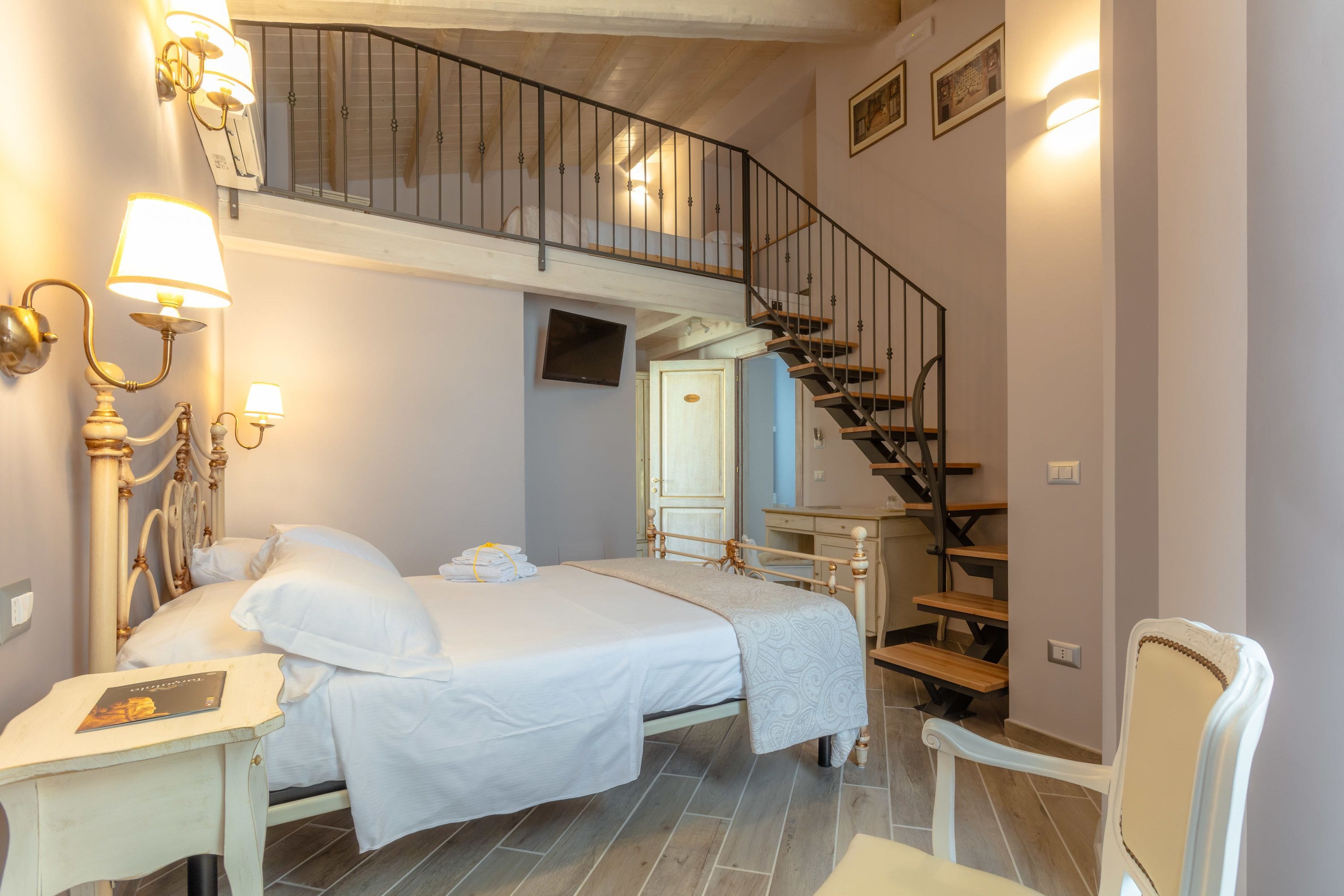 A bedroom with a double bed, a desk, a chair, a staircase, and a TV.