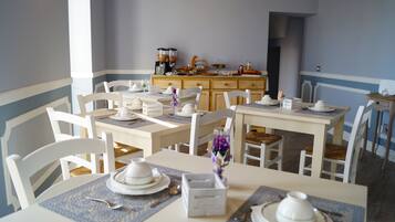 Zona pranzo con sedie e tavoli bianchi, un mobiletto per buffet in legno e un vaso con fiori viola.
