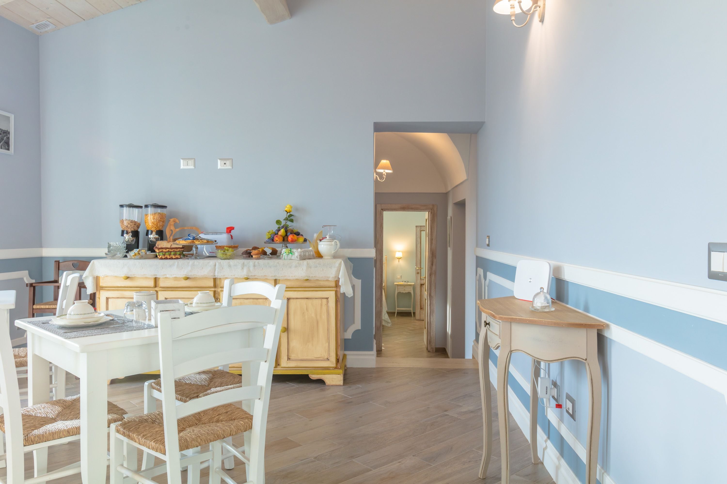 Un comedor con mesa y sillas de madera, una encimera de cocina con alimentos, y un pasillo que conduce a otra habitación.