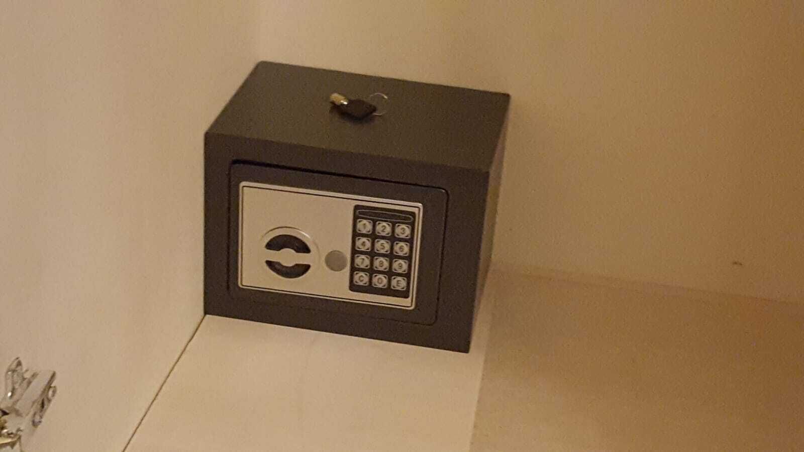 Una caja fuerte metálica segura con cerradura numérica, ubicada frente a una pared lisa.