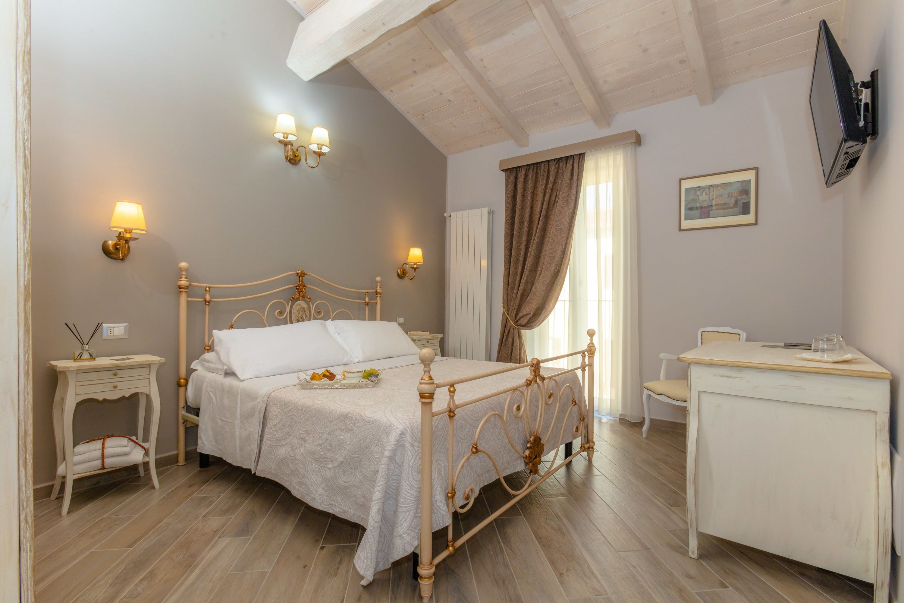 A bedroom with a bed, bedside tables, a desk, and a TV mounted on the wall.