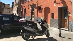 Ein Gebäude mit roter Fassade, davor ein schwarzes Auto und ein Roller.