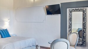 A bedroom with a bed, two chairs, a TV, and a large mirror. - B&B Palazzo del Magnifico (Siena)