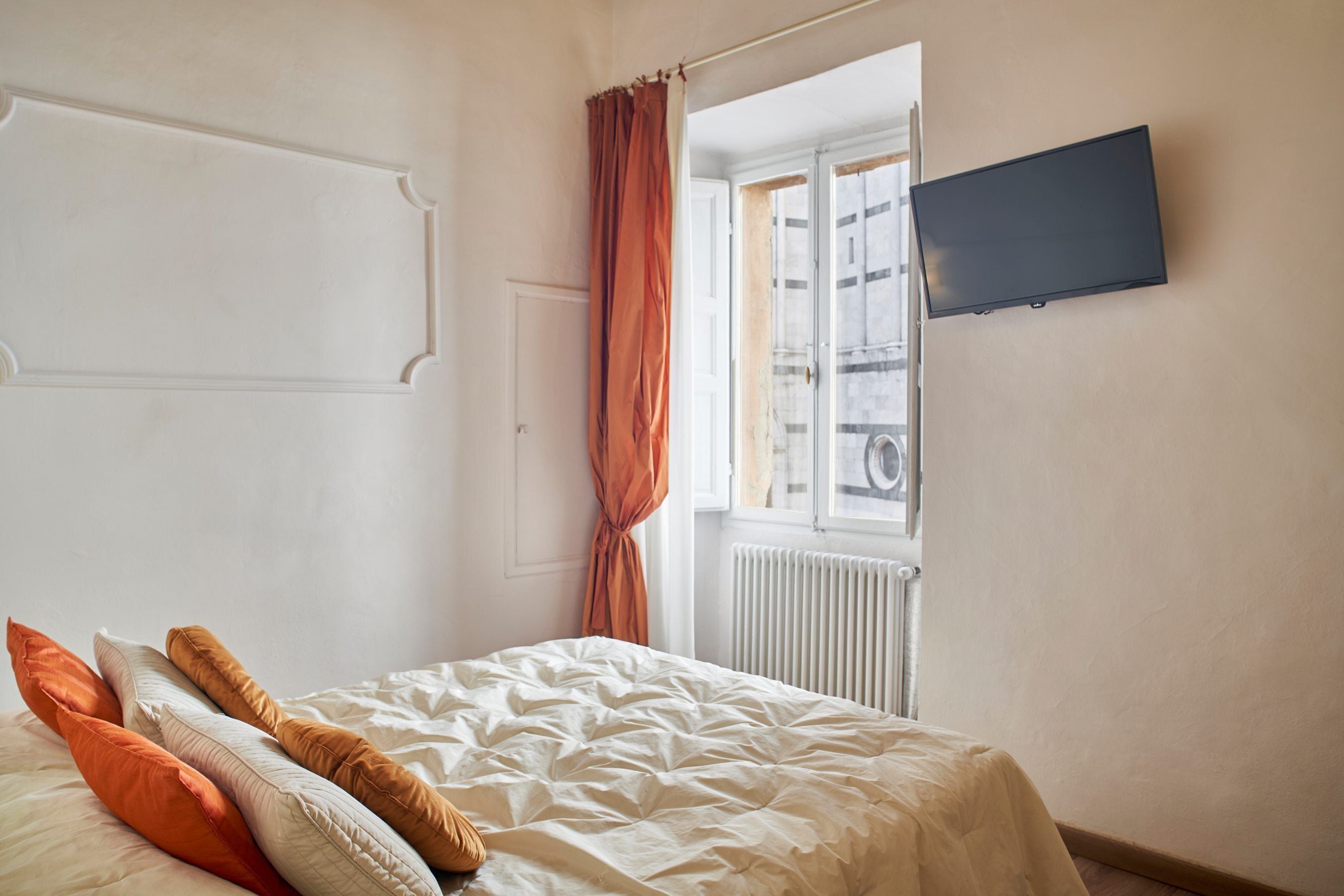 A bedroom with a bed, pillows, a window, and a wall-mounted TV.