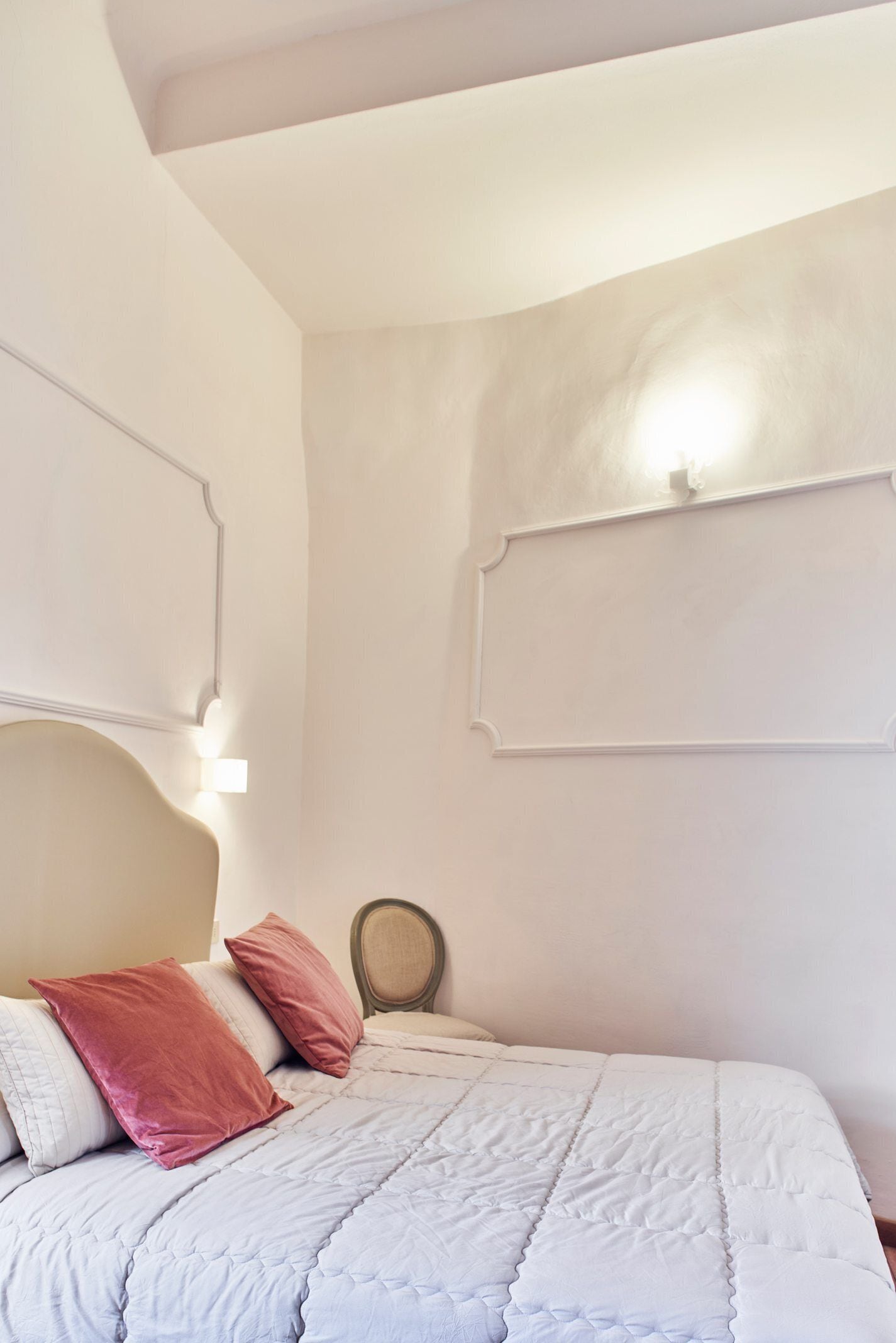 A bedroom with a bed, pillows, a headboard, and wall-mounted light fixtures.