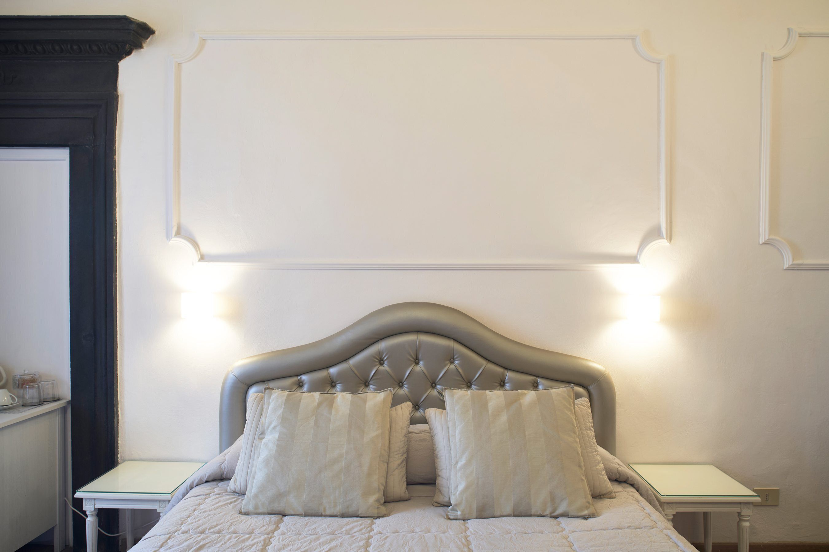 A neatly made bed with a tufted headboard, two bedside tables, and a wall-mounted light fixture above the bed.