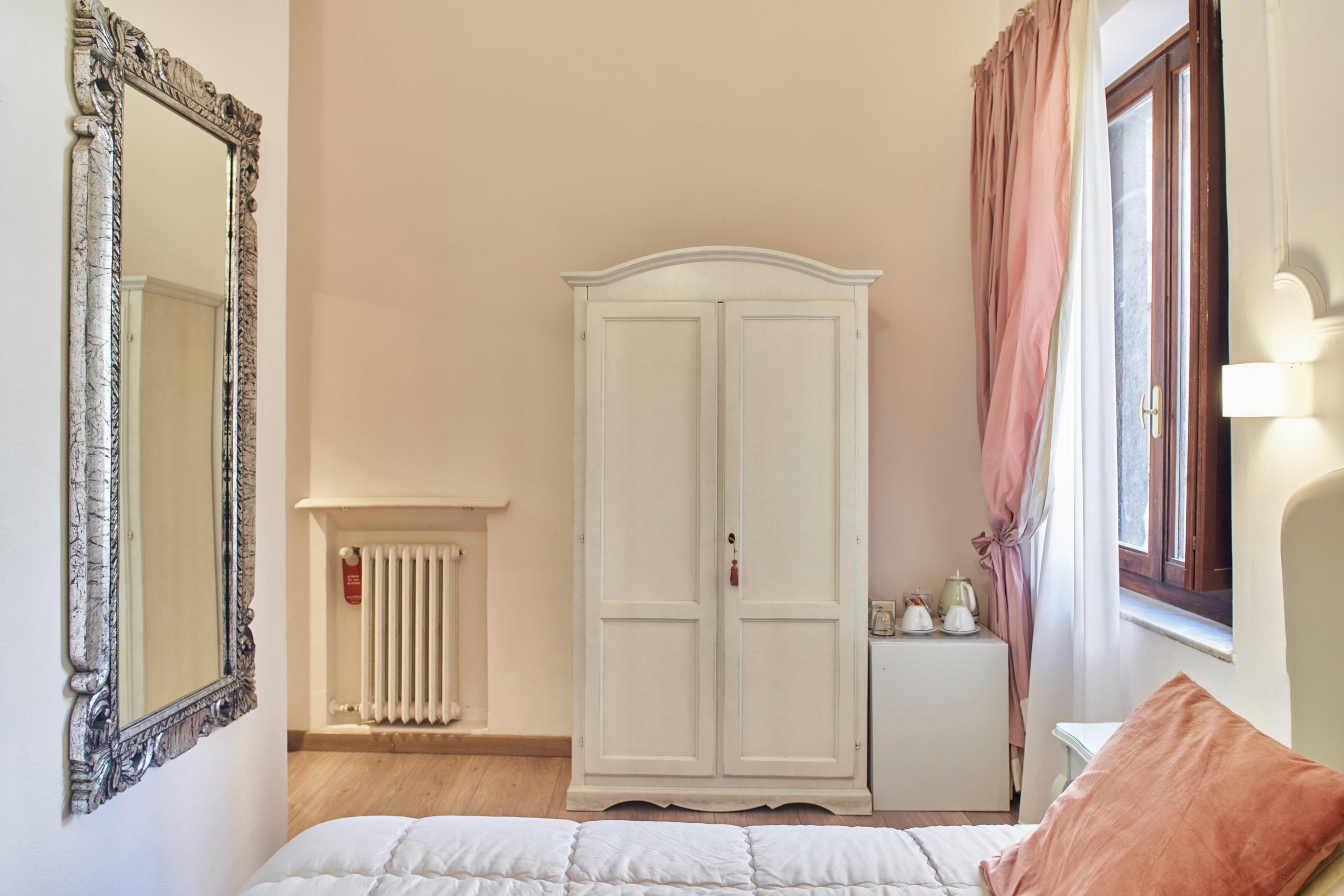 Ein Schlafzimmer mit Bett, Kleiderschrank, Heizkörper, Nachttisch und einem Fenster mit Vorhängen.