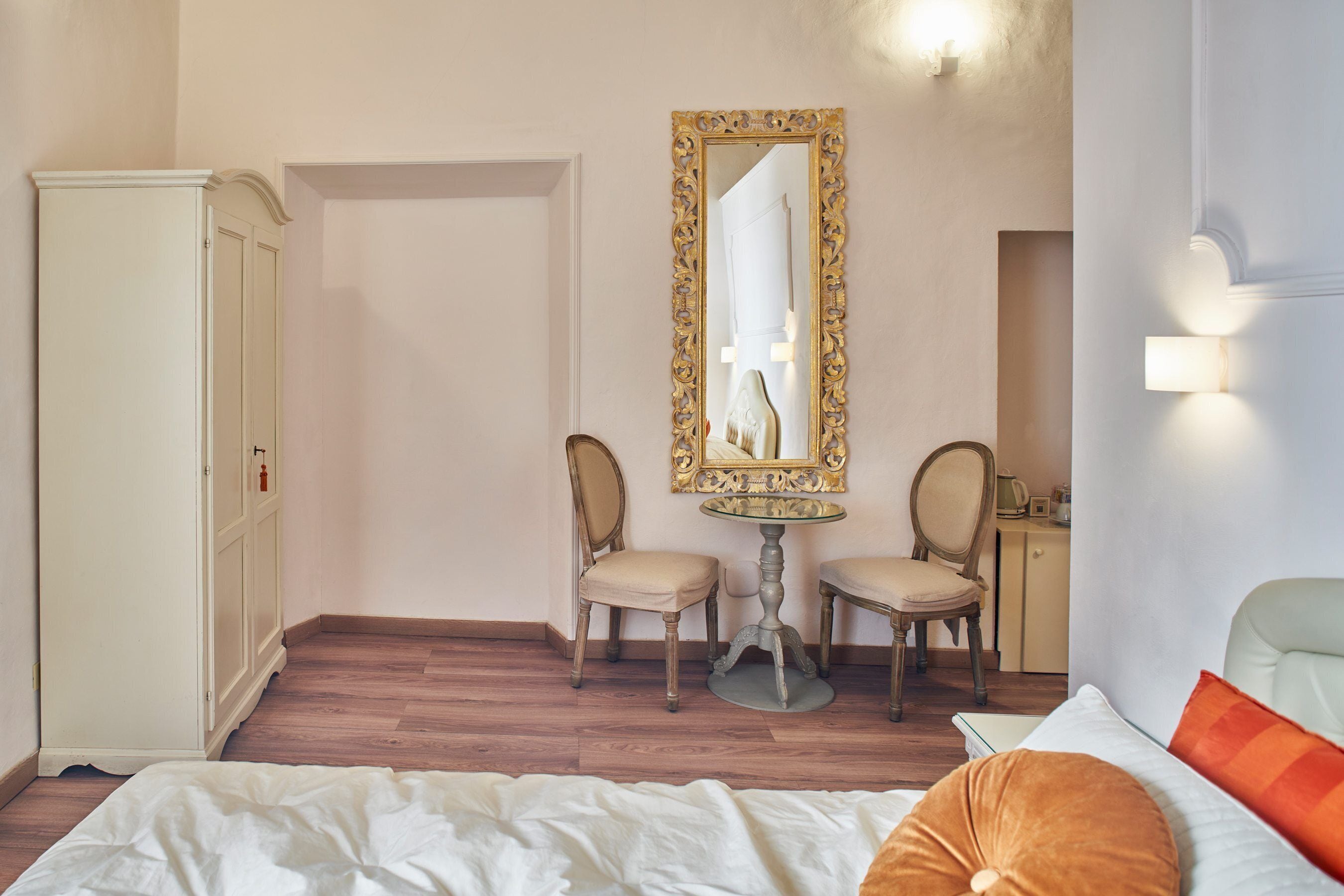 Ein Schlafzimmer mit einem Bett, zwei Stühlen, einem kleinen Tisch, einem Spiegel und einem Kleiderschrank.