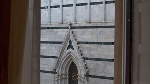 A window with a view of a building's exterior, featuring a patterned facade and a gothic archway. - B&B Palazzo del Magnifico (Siena)