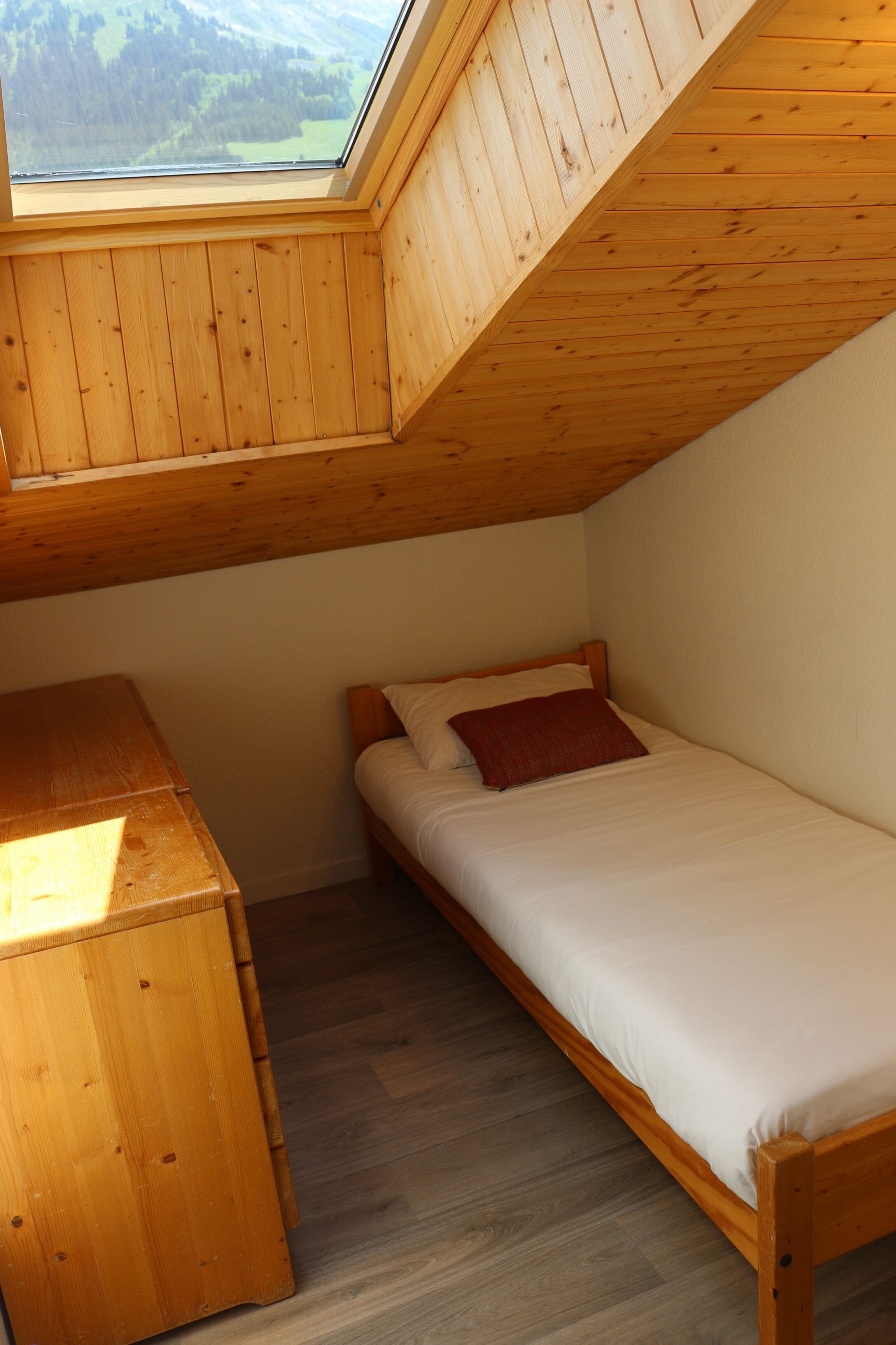 Una cabaña pequeña de una sola habitación con techo inclinado, un escritorio de madera, una cama individual y un tragaluz.