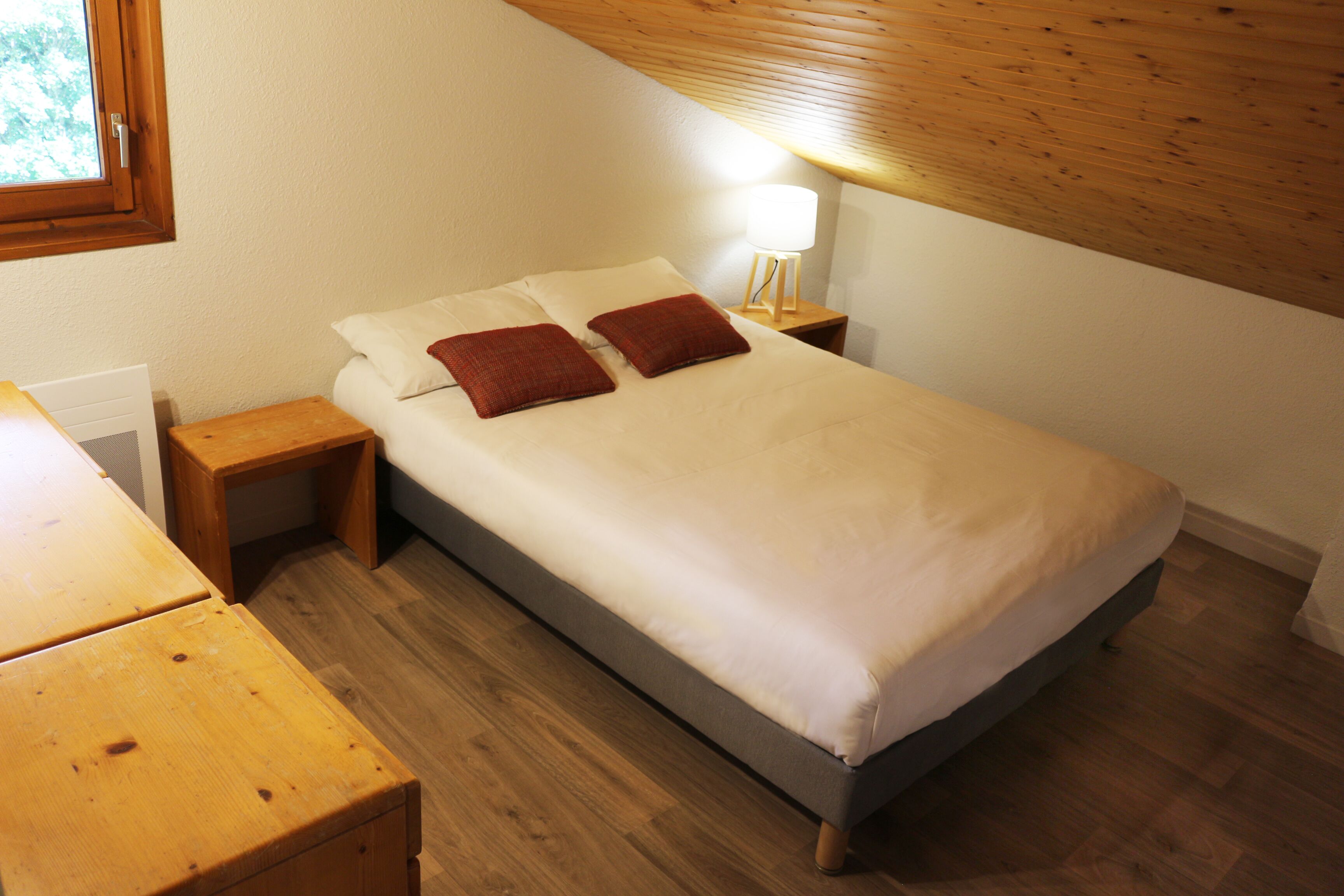 A neatly made bed with two pillows, a bedside table, and a nightstand with a lamp.